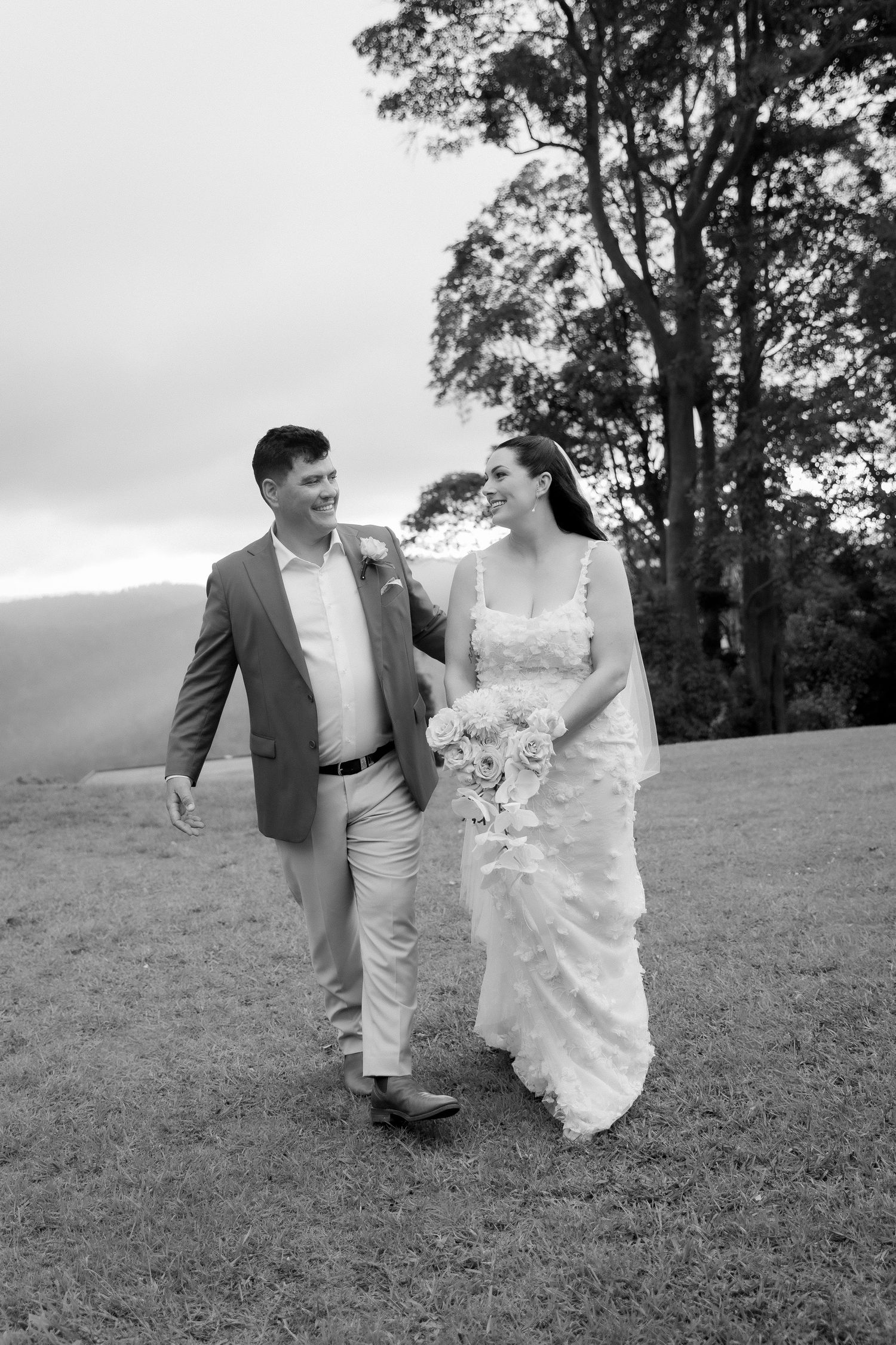Bride and groom walking together on misty hillside in black and white wedding photo.