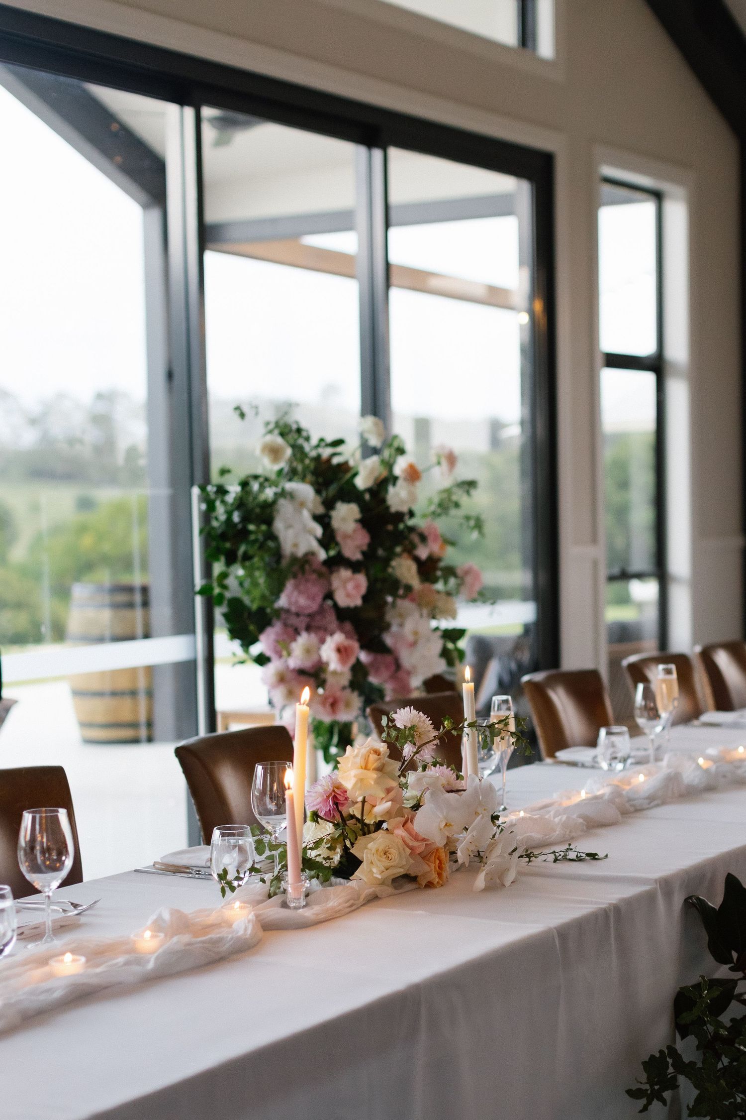 Elegant wedding reception table with floral centerpieces, candles, and white linens in a modern venue.
