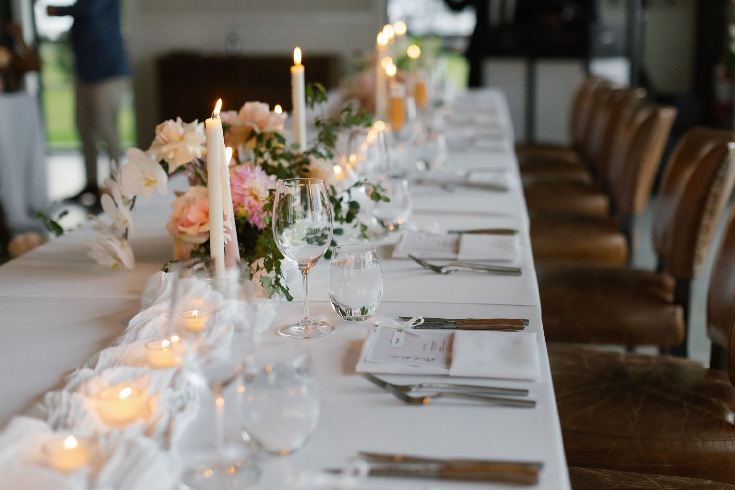 Elegant wedding reception table with candles, pink floral centerpieces, and white linen settings.