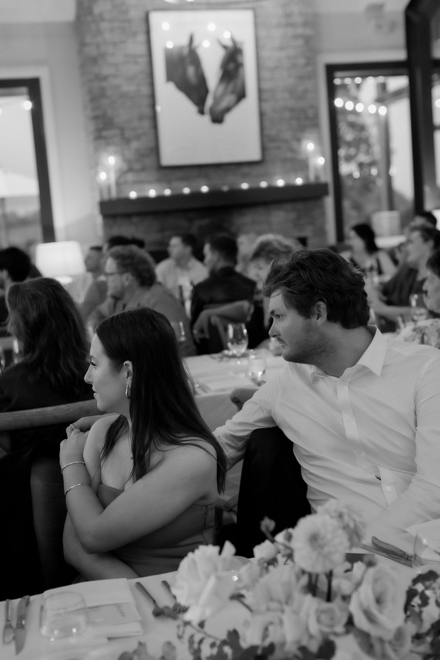 Black and white photo of couple sitting together at candlelit wedding reception dinner table.