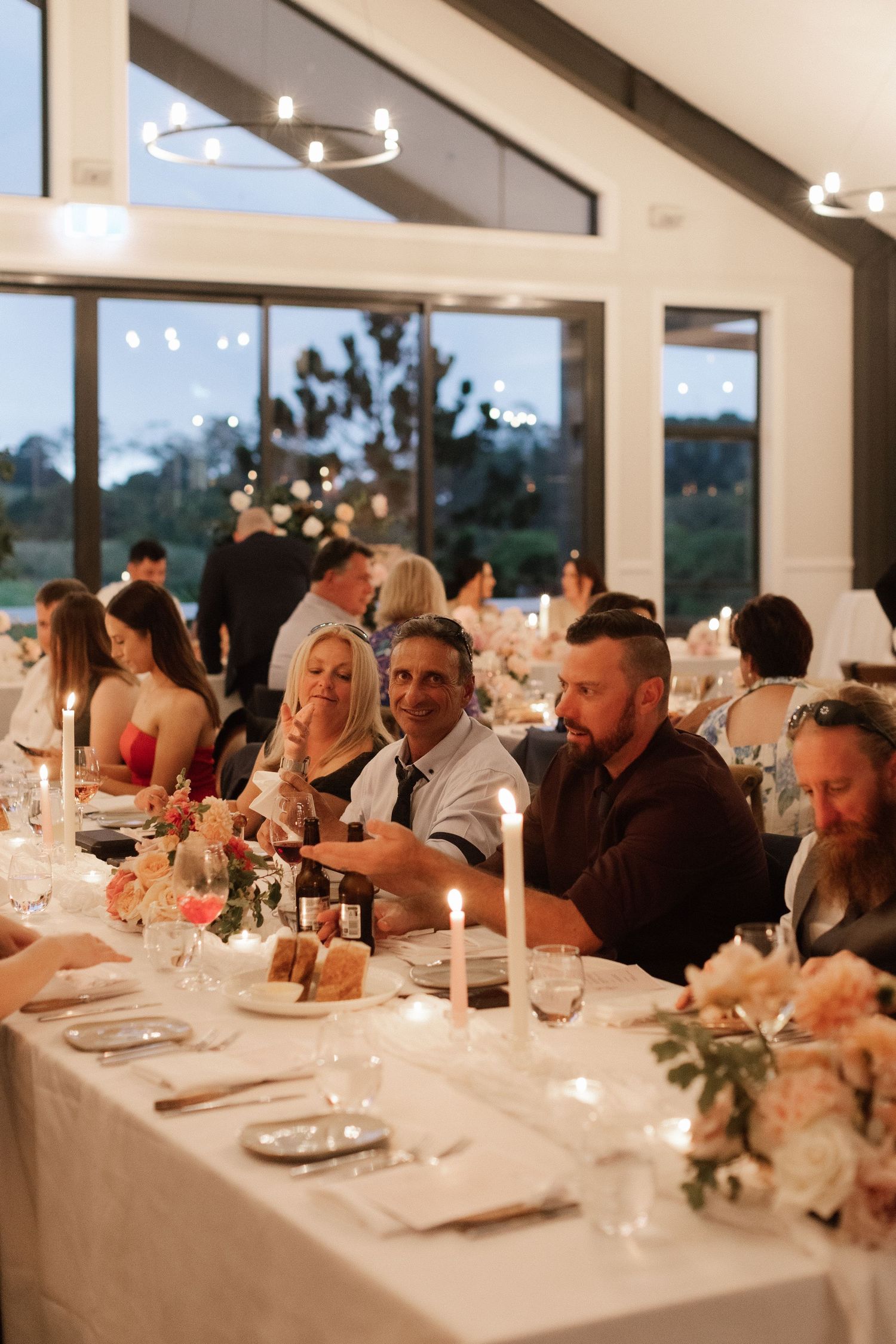 Wedding reception guests seated at candlelit tables in elegant evening venue.