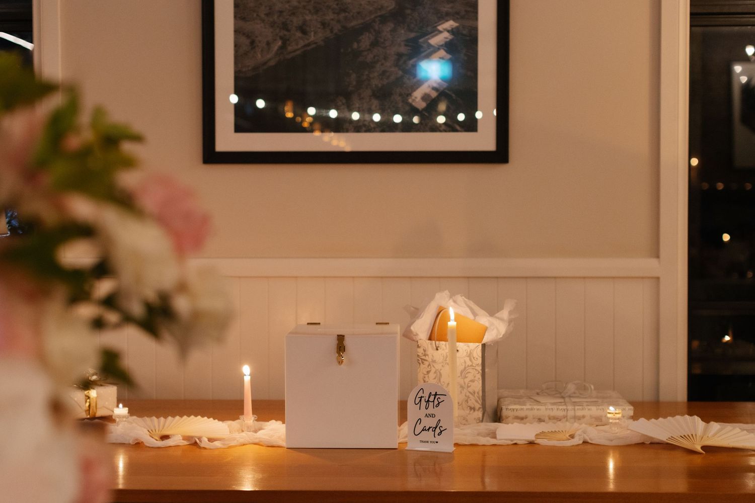Wedding gift table with white card box, candles, and gift bag in warmly lit room.