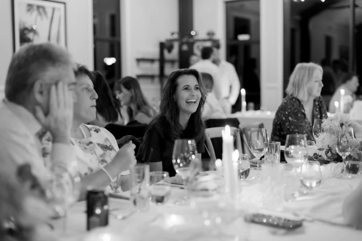 Black and white photo of a wedding guest laughing joyfully during the reception dinner.