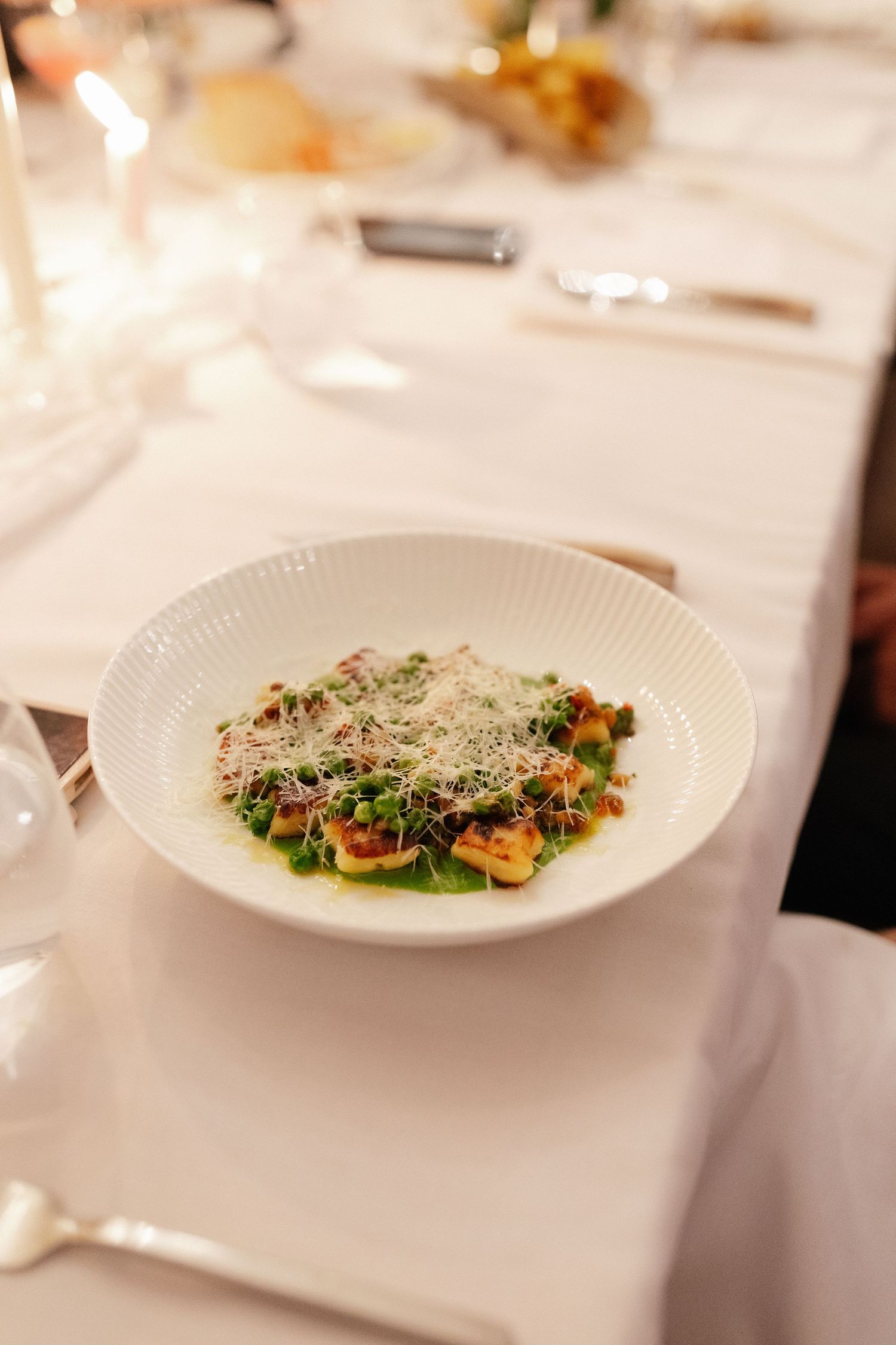 Elegant fine dining dish with green pea puree, gnocchi, and shaved parmesan in a white bowl on a formal table.