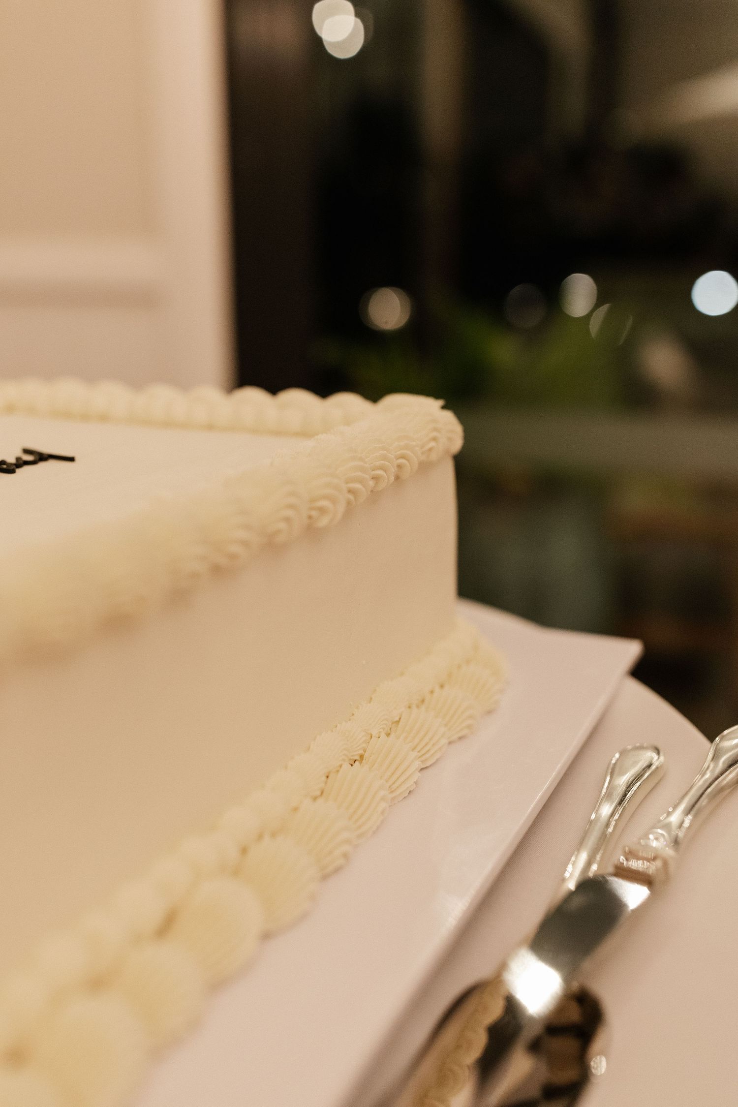 Elegant white wedding cake with pearl and rosette piping details, served with a silver cake knife.