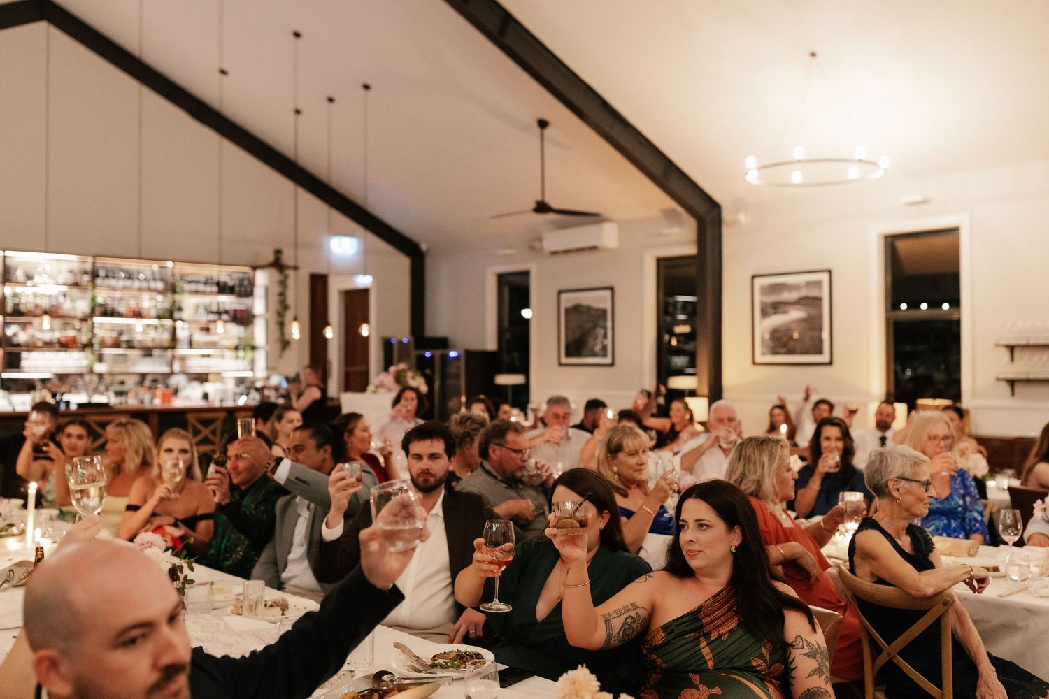 Guests raise glasses during a wedding reception dinner in an elegant restaurant venue.