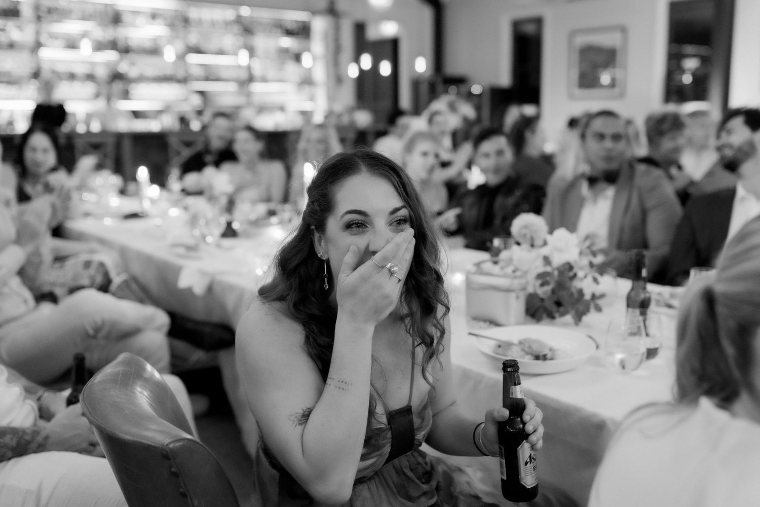Black and white photo of a wedding guest covering her mouth in surprise during reception speeches.