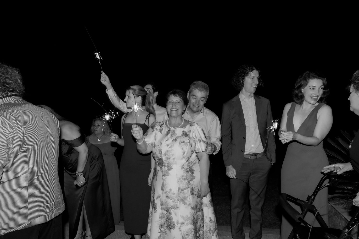 Black and white photo of wedding guests holding sparklers at night outdoor celebration.