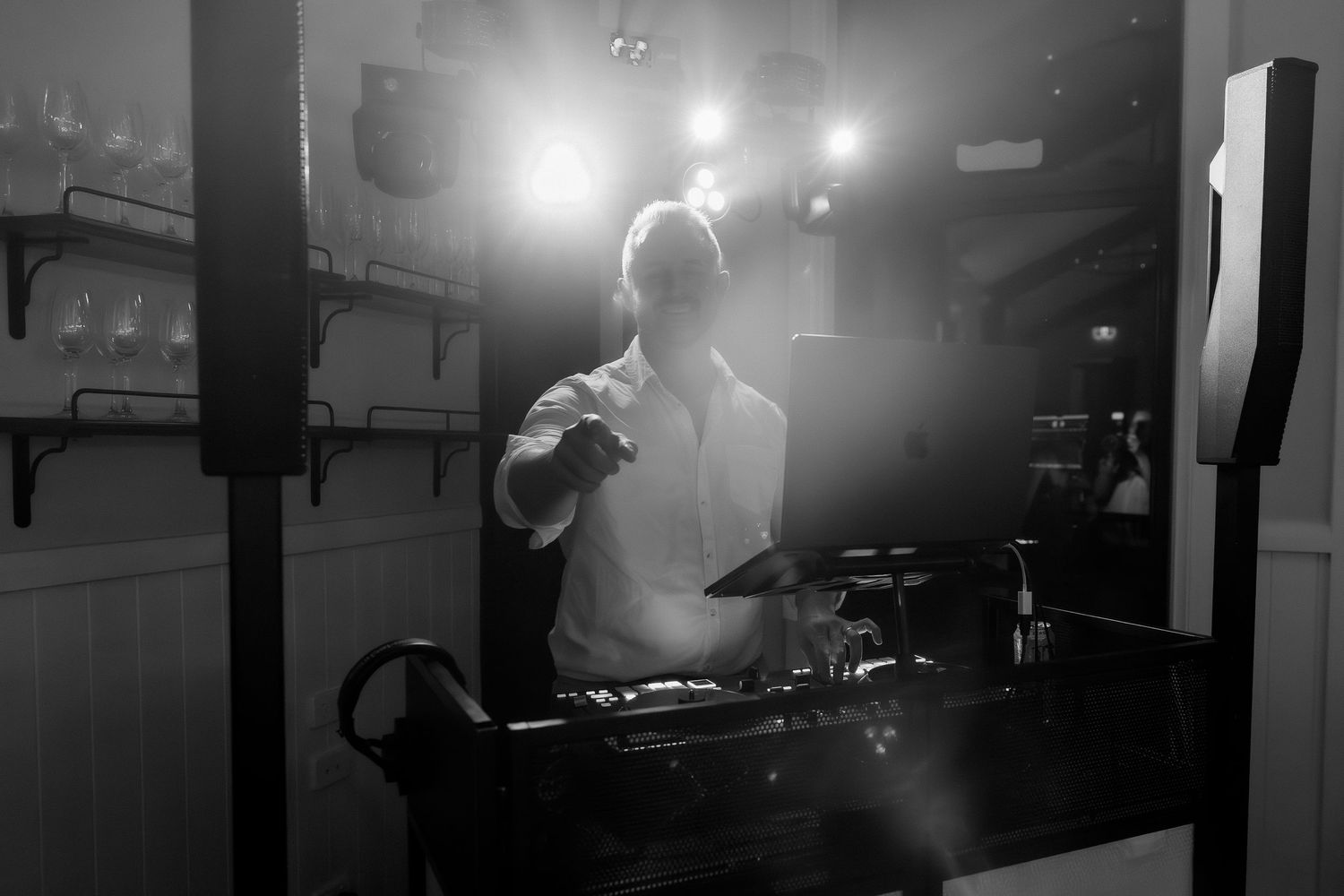 Black and white photo of a DJ performing at a wedding reception with dramatic lighting.