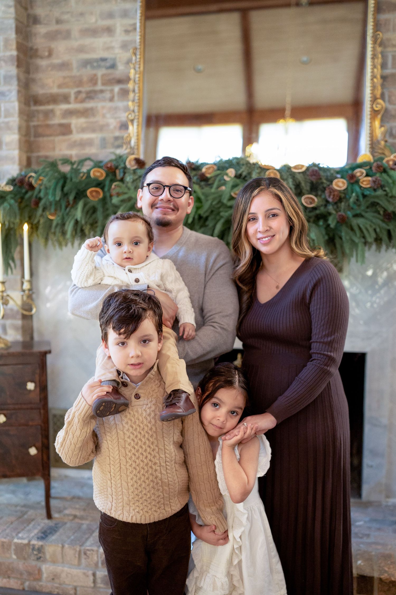 Family of five posing for a Christmas portrait in front of a festive garland-decorated fireplace mantel. Cinnamon Sugar Christmas photos