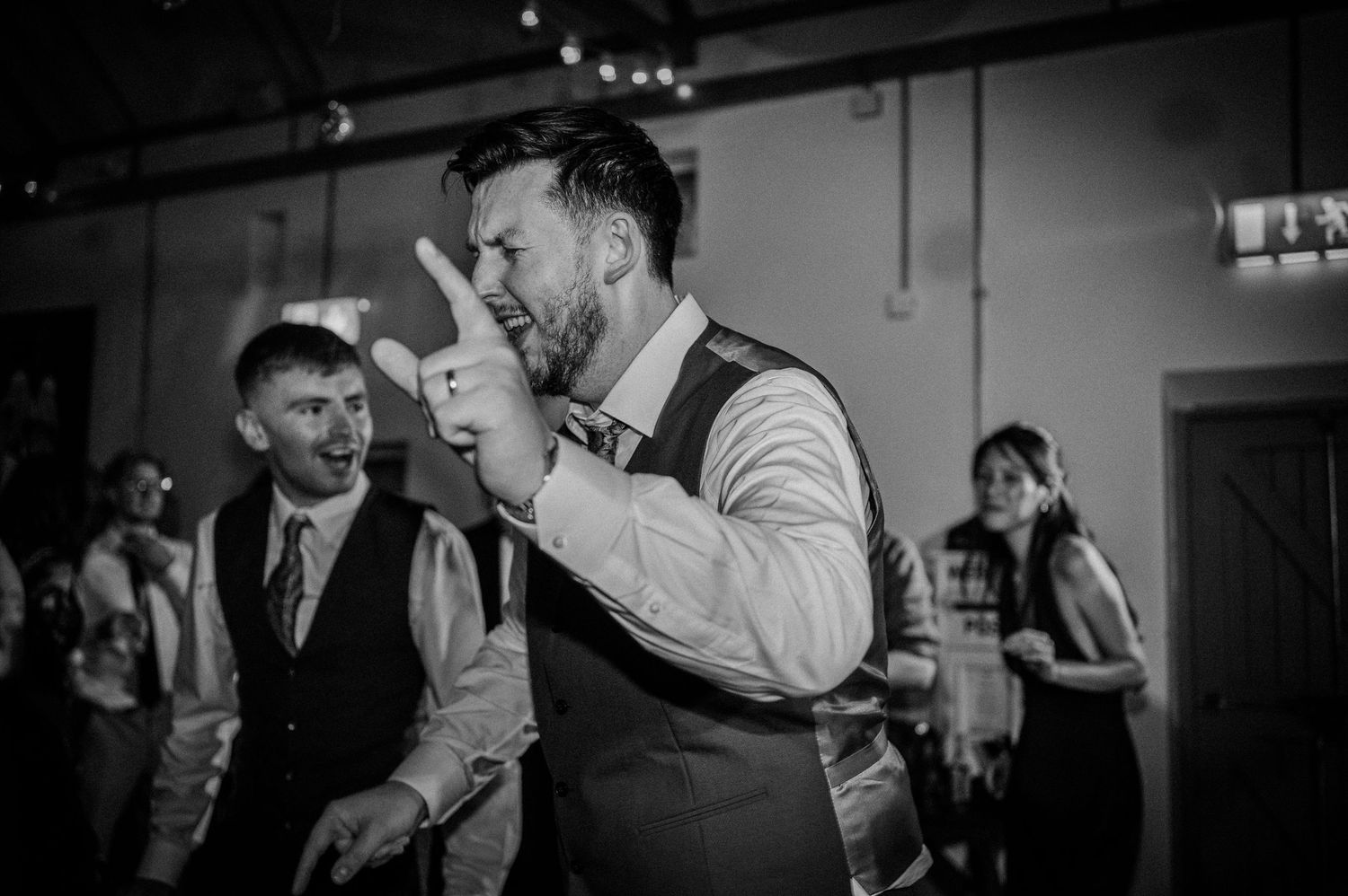 Man energetically dancing and pointing finger at wedding reception party in black and white photo.