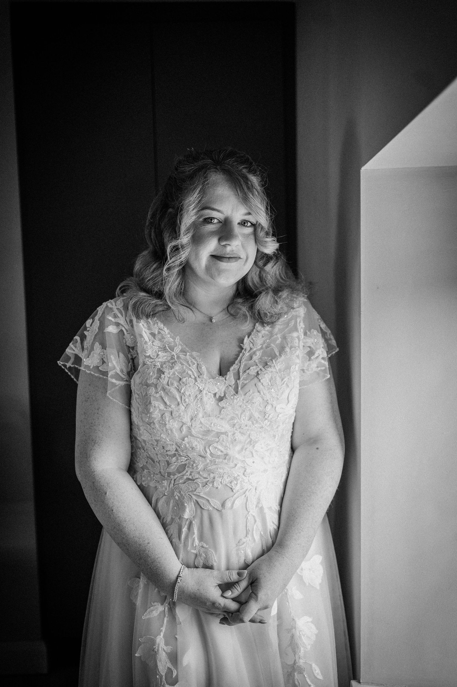 Bride in lace wedding dress posing elegantly in black and white portrait photo.