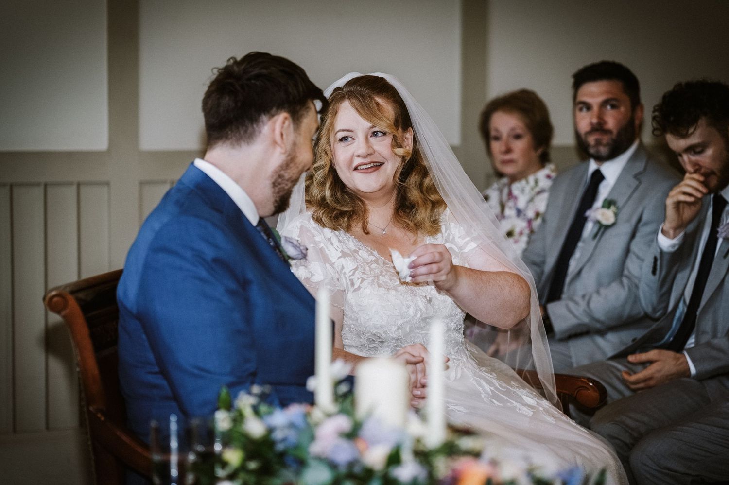 Smiling bride in lace dress shares a joyful moment with groom during wedding ceremony.