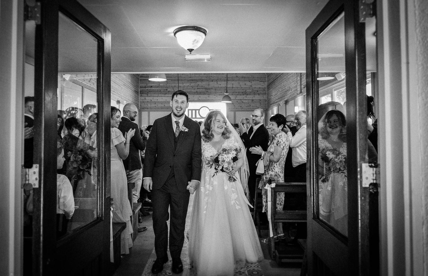Black and white photo of a bride and groom walking down the aisle at their wedding ceremony.