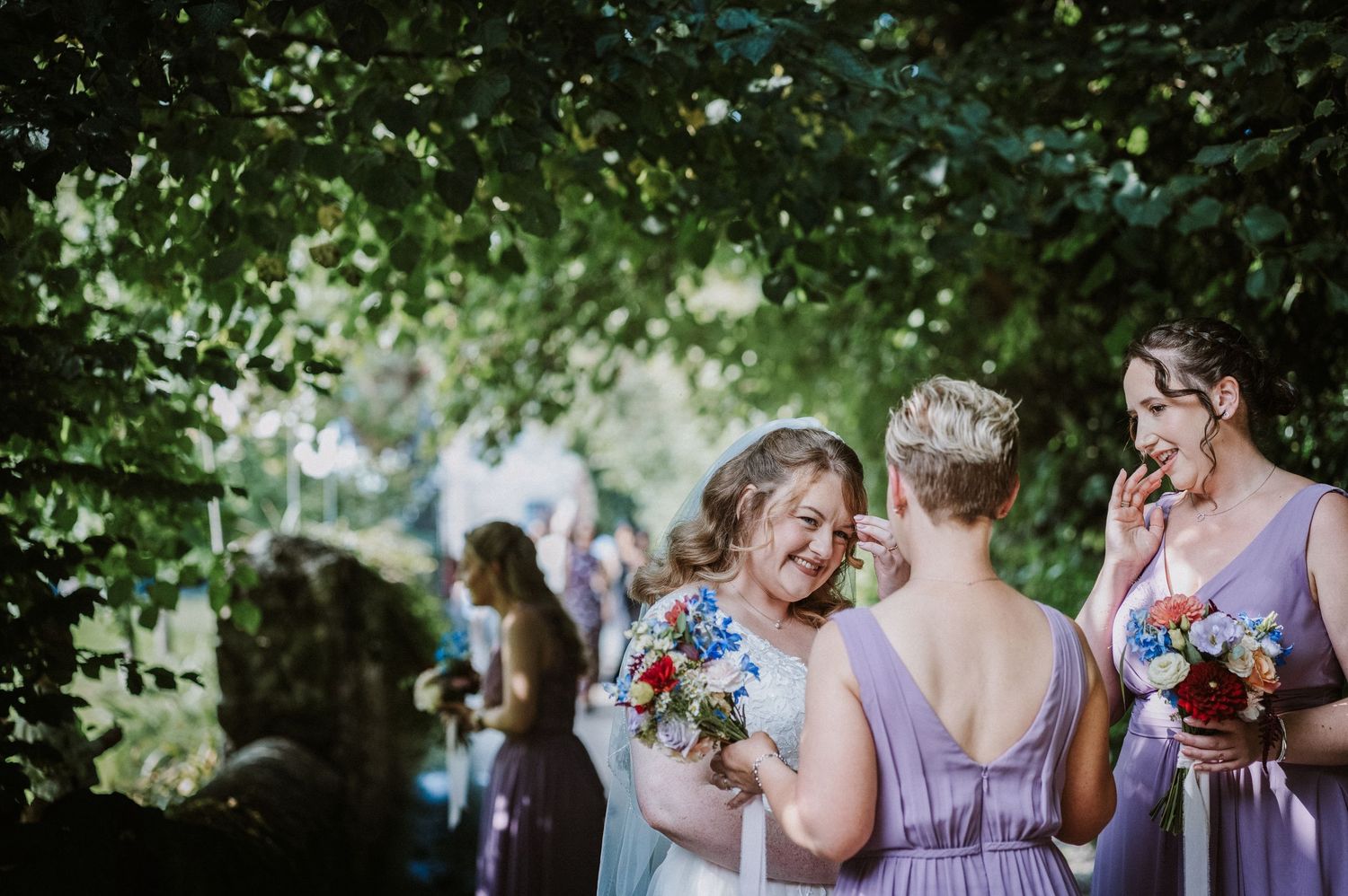 Bridesmaids in lavender dresses laughing together outdoors at a wedding reception.