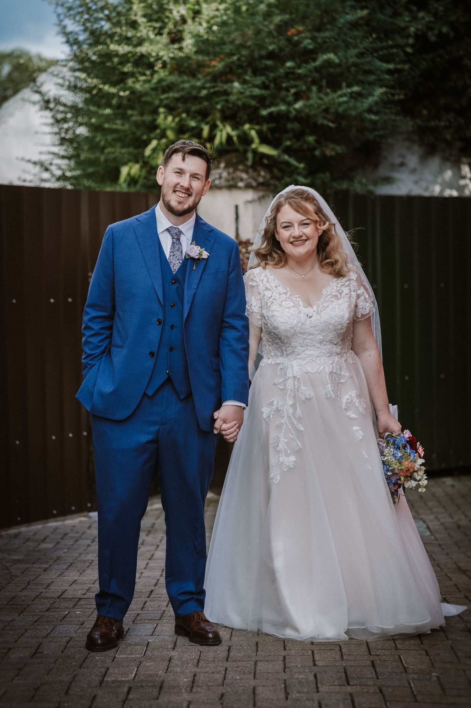 Bride and groom pose together outdoors, holding hands in wedding attire on their special day.
