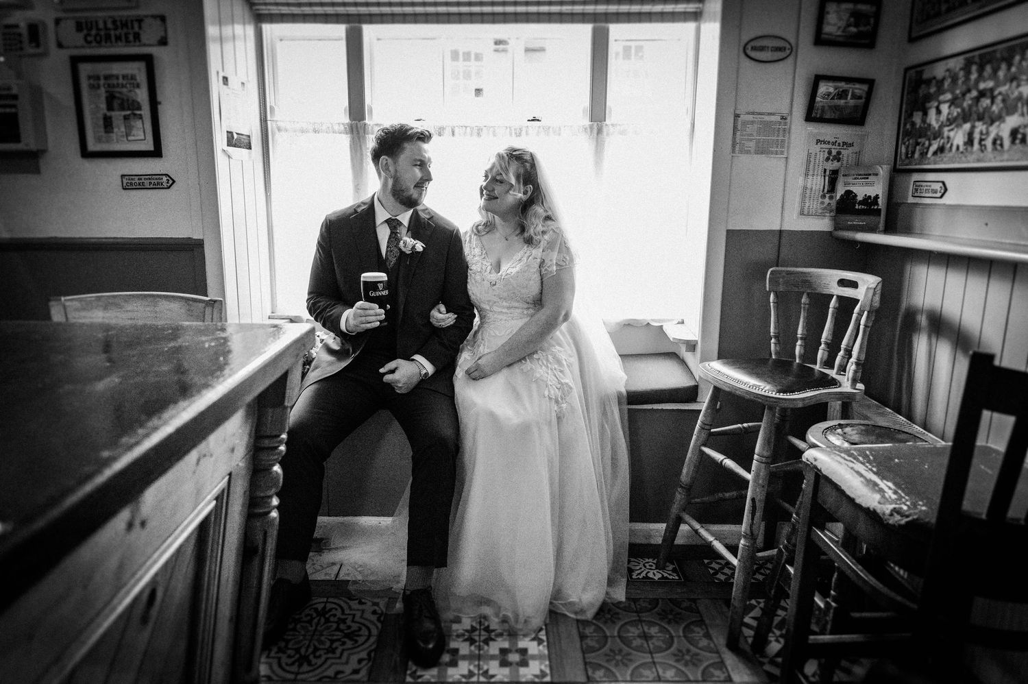 Black and white photo of bride and groom sharing a quiet moment together at a pub bar by a window.