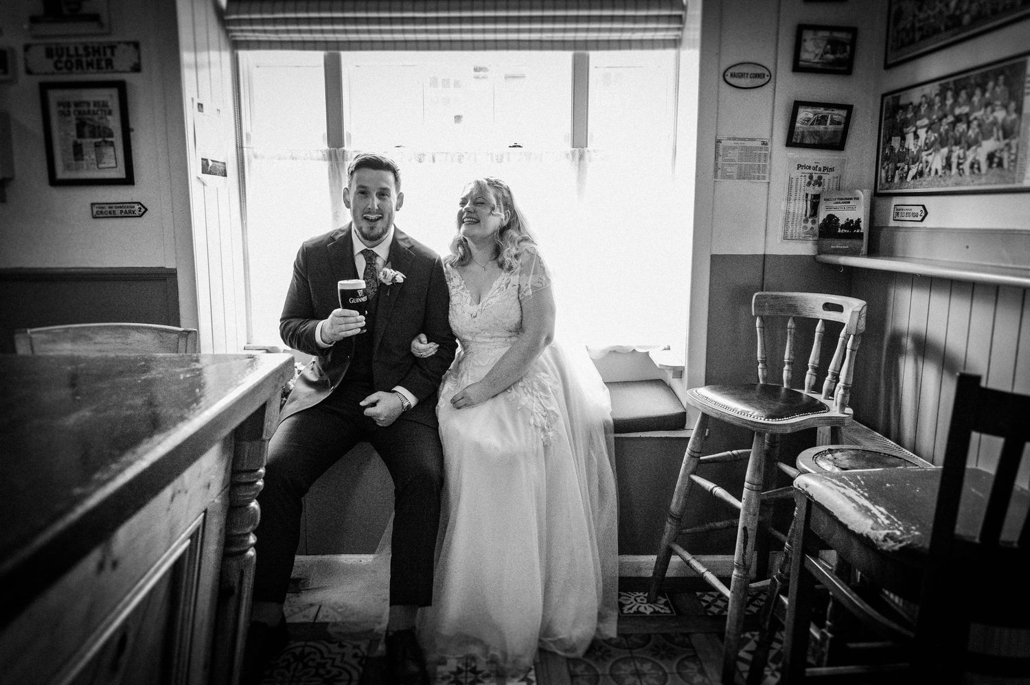 Bride and groom laugh together inside rustic venue bar on their wedding day.