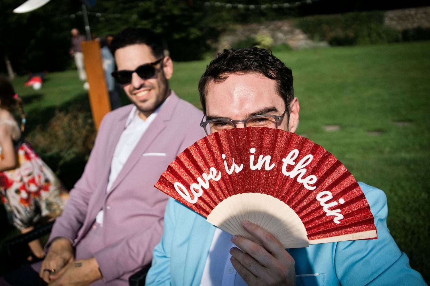 Wedding guest holds red fan reading love is in the air at outdoor reception.