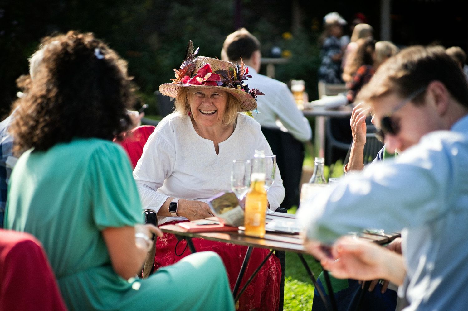 Wedding guest in a floral hat laughing at an outdoor garden reception table.