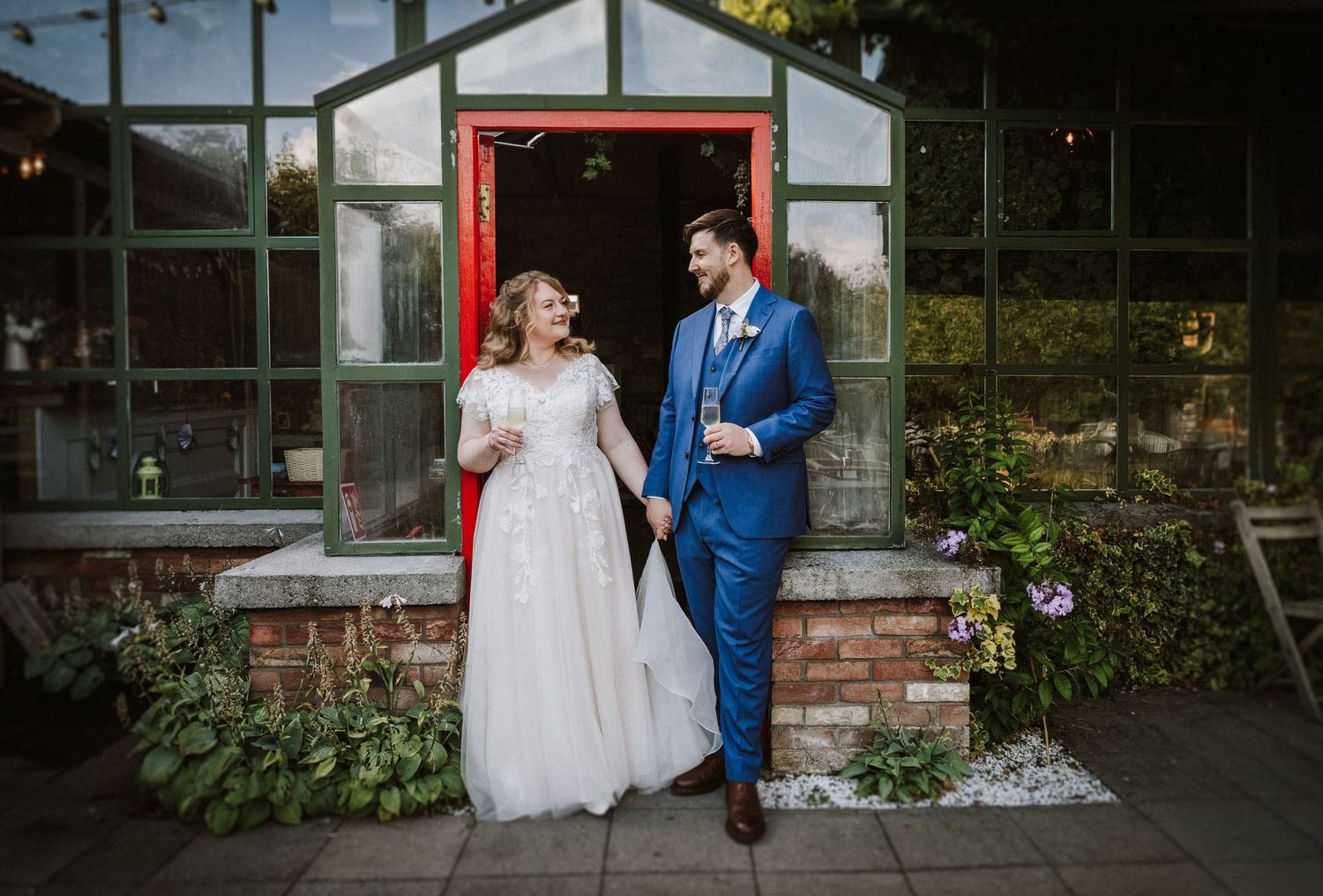 Bride and groom laughing together outside a greenhouse venue on their wedding day.
