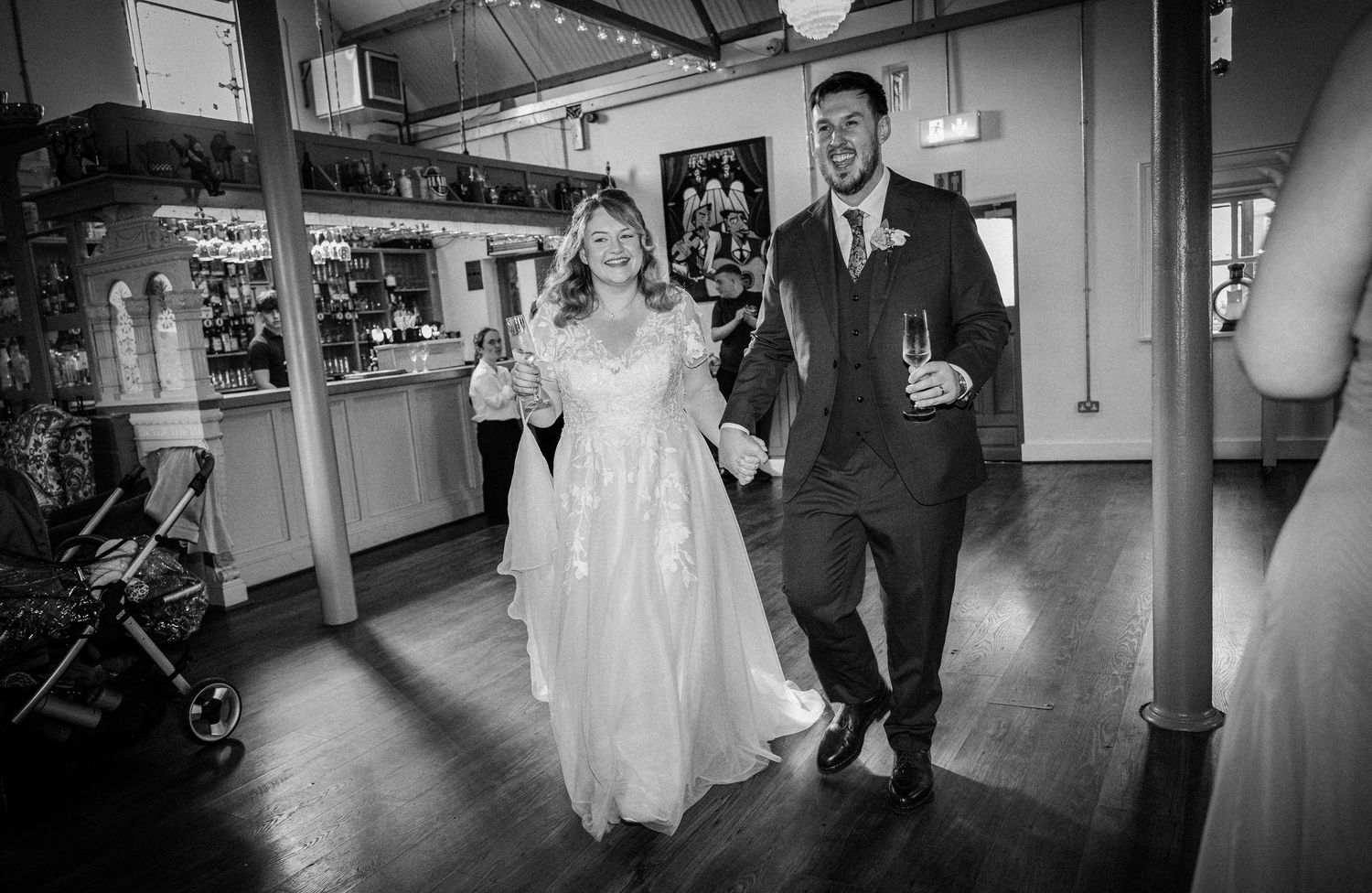 Bride and groom walking hand in hand into wedding reception venue, smiling joyfully.