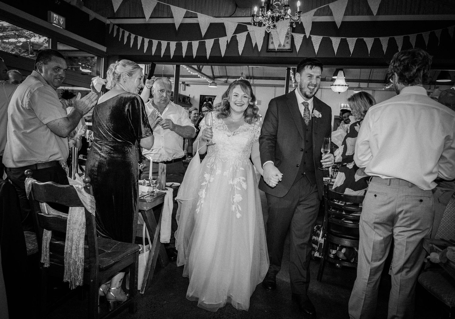 Bride and groom make joyful entrance through dancing wedding guests in black and white.