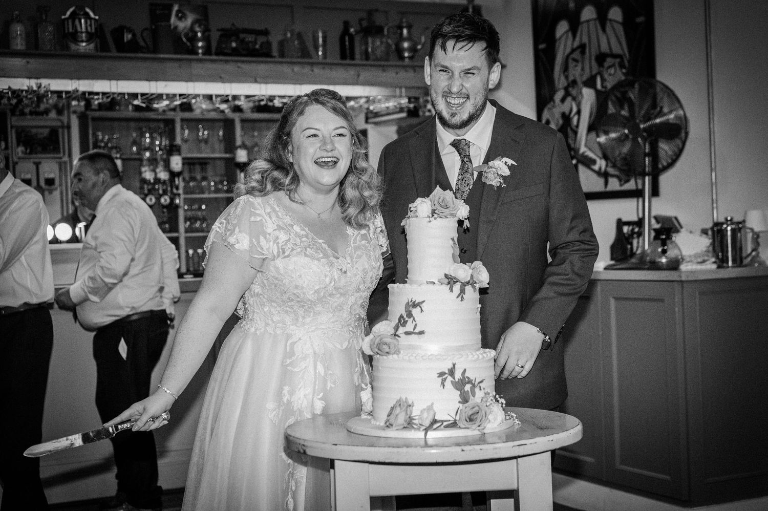 Bride and groom smile while cutting their elegant white tiered wedding cake together.