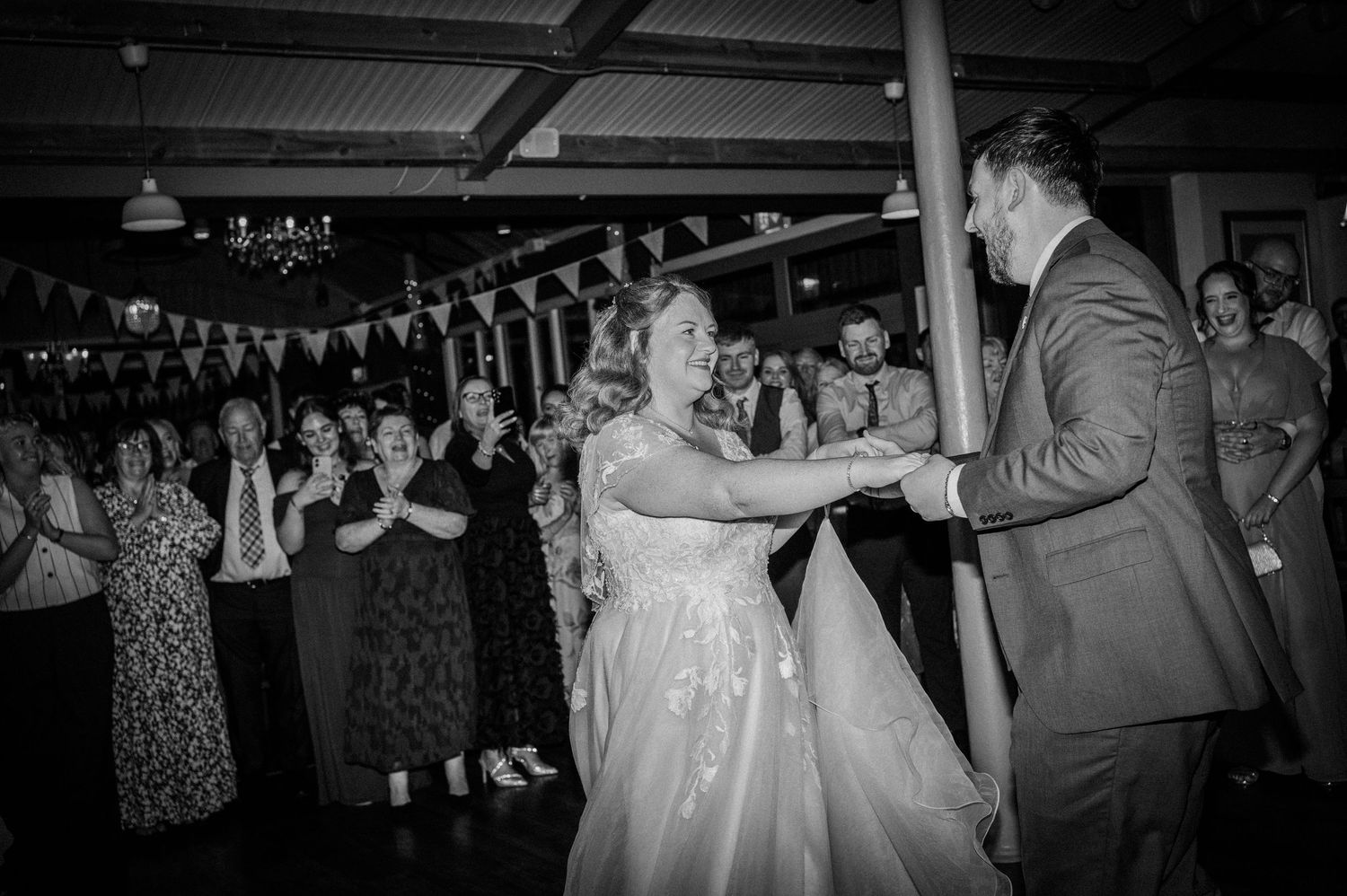 Bride and groom share their first dance surrounded by applauding wedding guests.