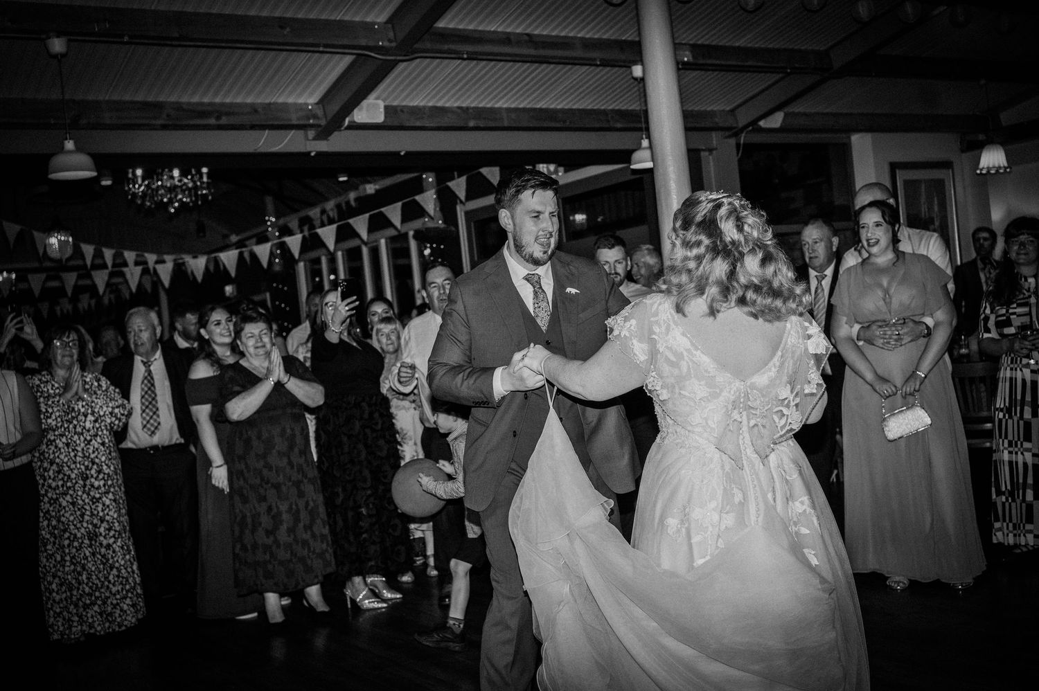 Bride and groom dance joyfully together as wedding guests watch and celebrate around them.