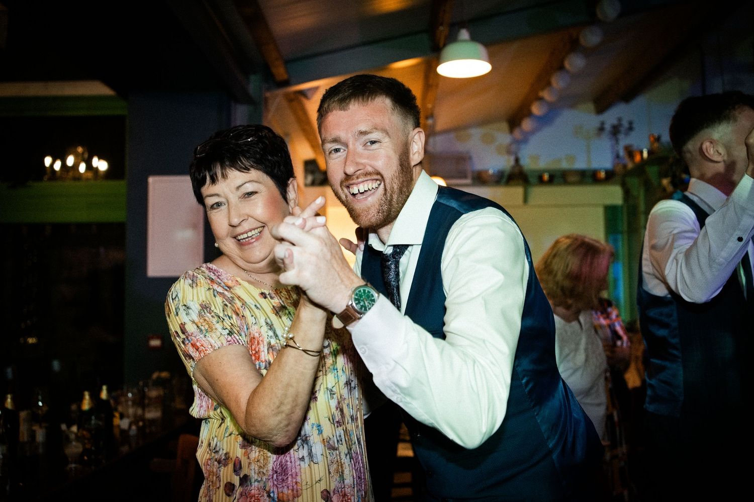Groom dances and laughs with a smiling female guest at the wedding reception.