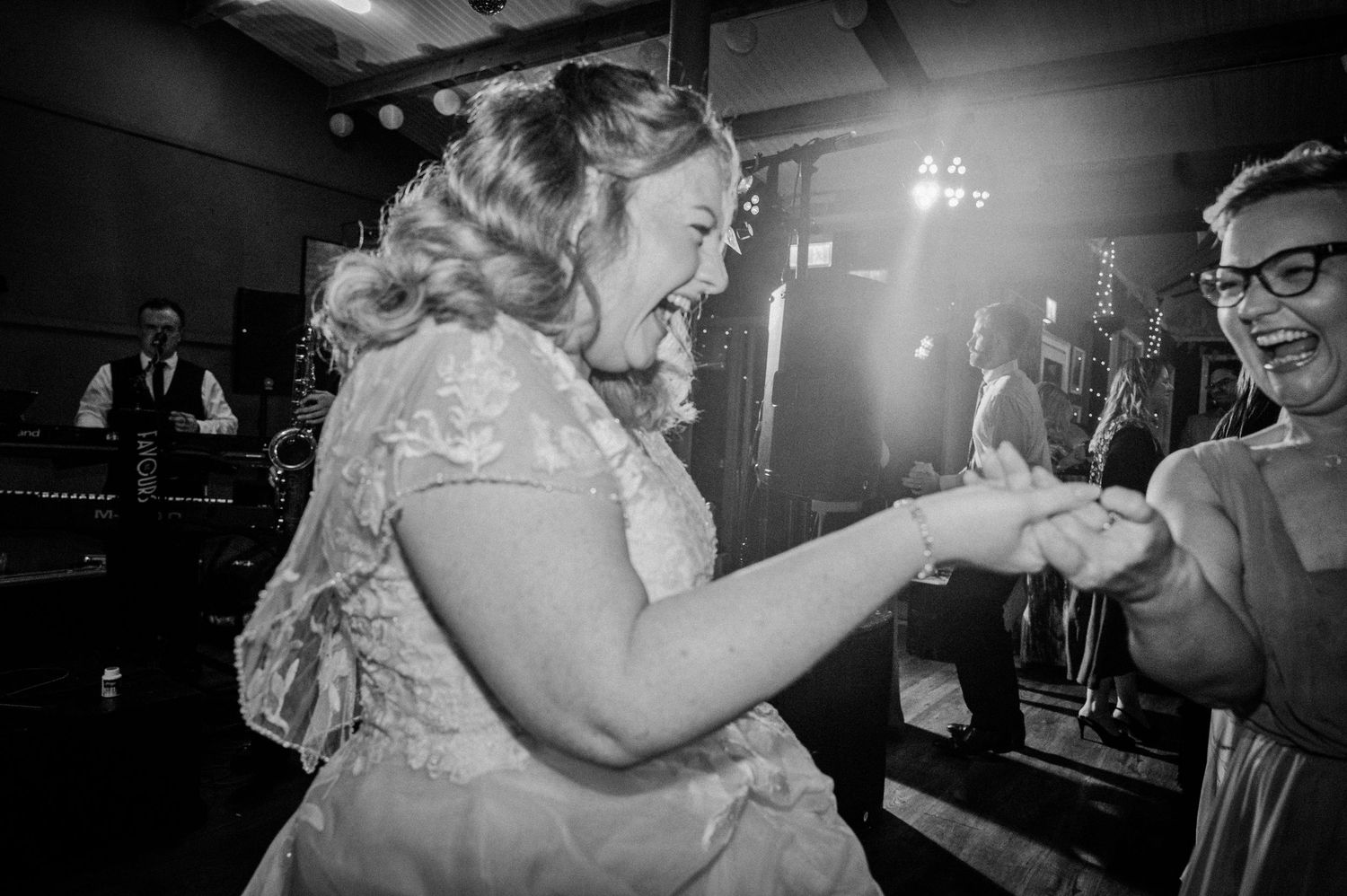 Bride laughs joyfully while dancing with a guest at a lively wedding reception.