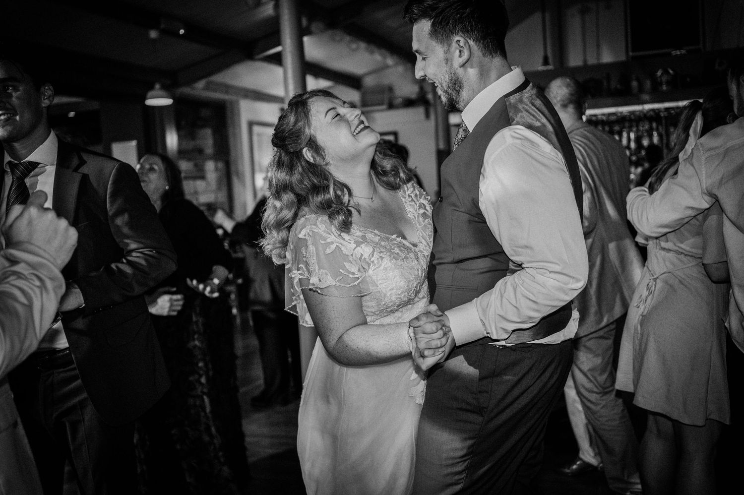Black and white photo of bride and groom laughing together while dancing at wedding reception.