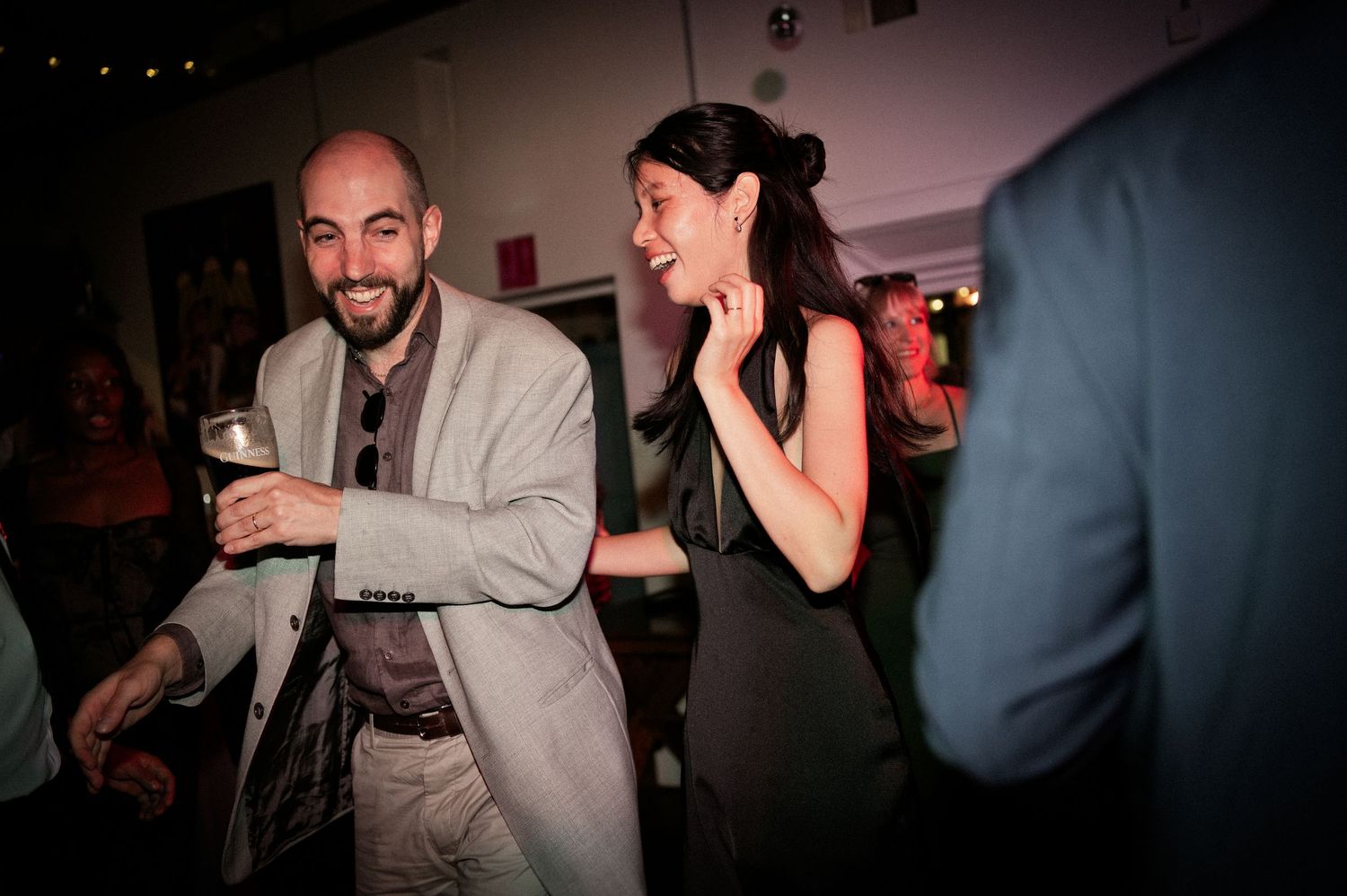 Smiling man in gray suit dances with laughing woman in black dress at elegant wedding reception.