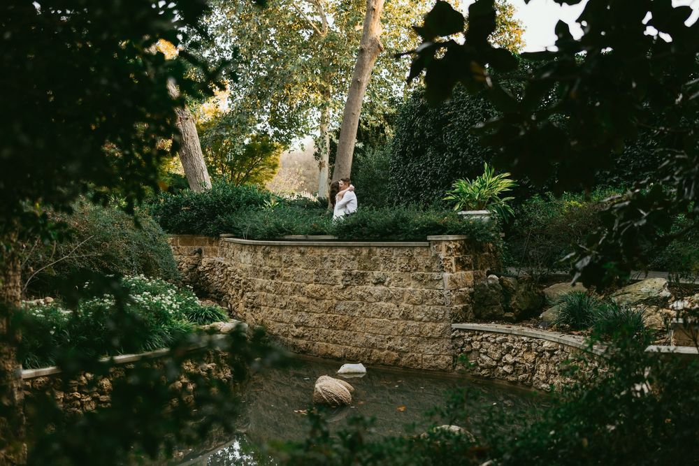 Couple embracing on a stone terrace surrounded by lush greenery in a romantic garden setting.