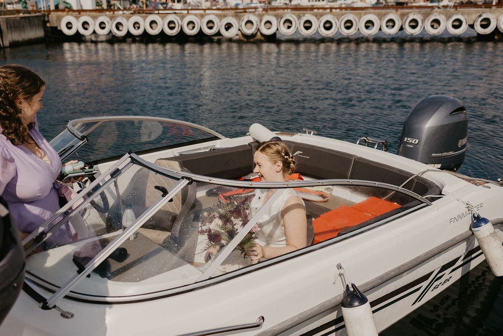 Young girl in a white dress sitting in a motorboat docked at a marina on a sunny day.