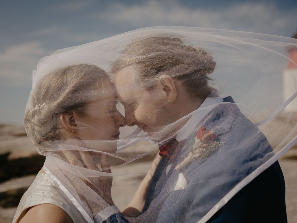 A bride and groom share an intimate moment under a flowing veil outdoors on their wedding day.