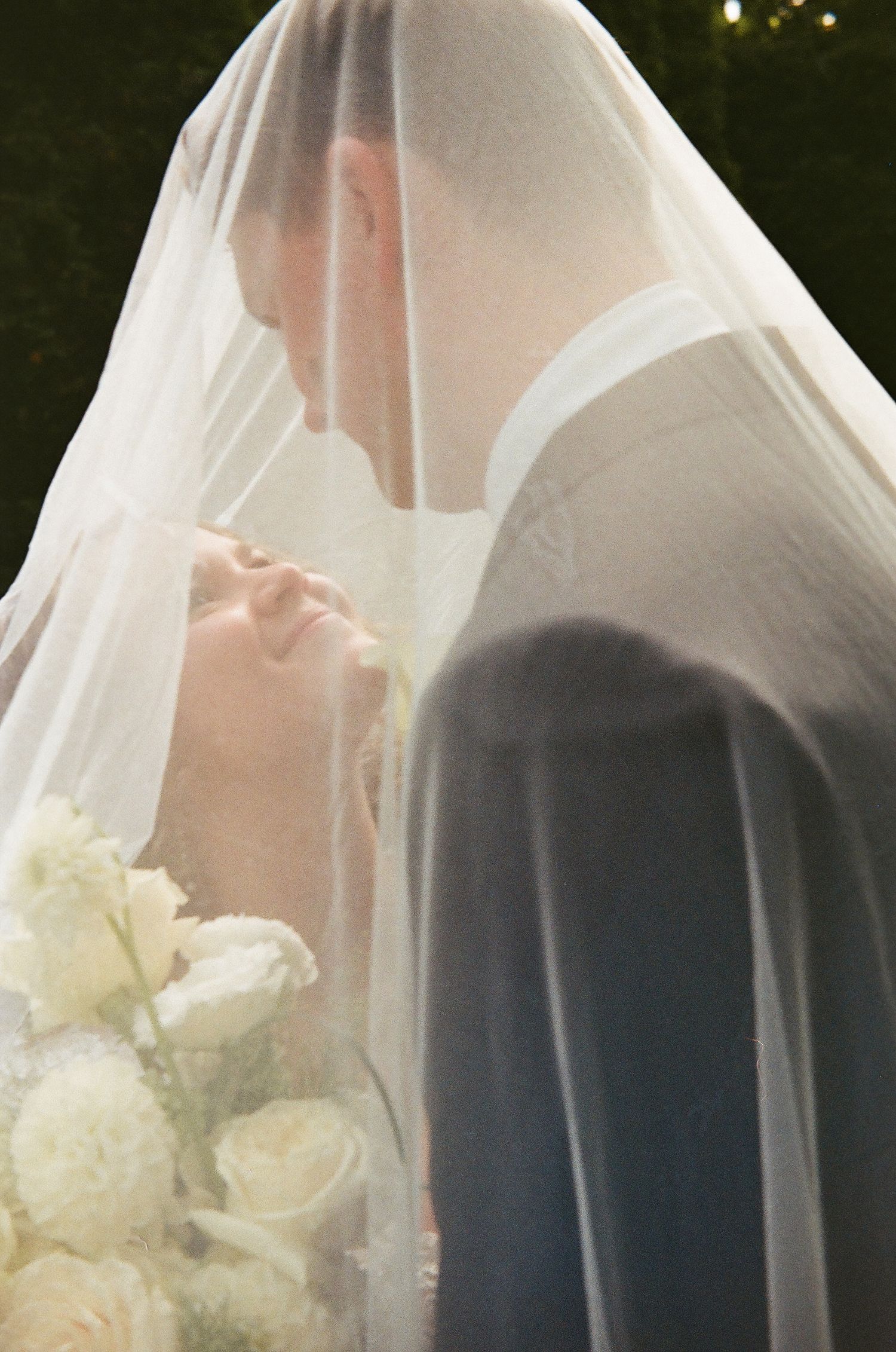 Bride and groom share an intimate moment under a sheer wedding veil, bride holding white roses bouquet.  Cranberry Creek Gardens Ontario