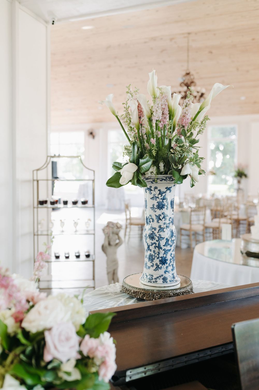 Blue and white chinoiserie vase with pink flowers and calla lilies displayed on a piano in an elegant event venue.