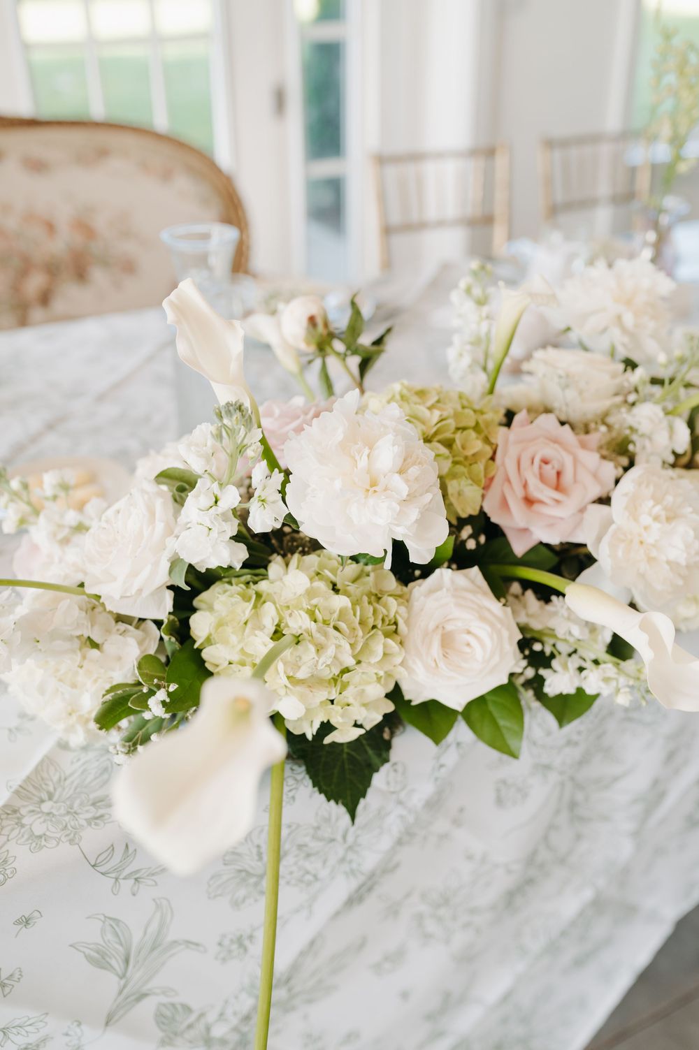 Elegant wedding centerpiece with white hydrangeas, blush roses, and calla lilies on a marble table.