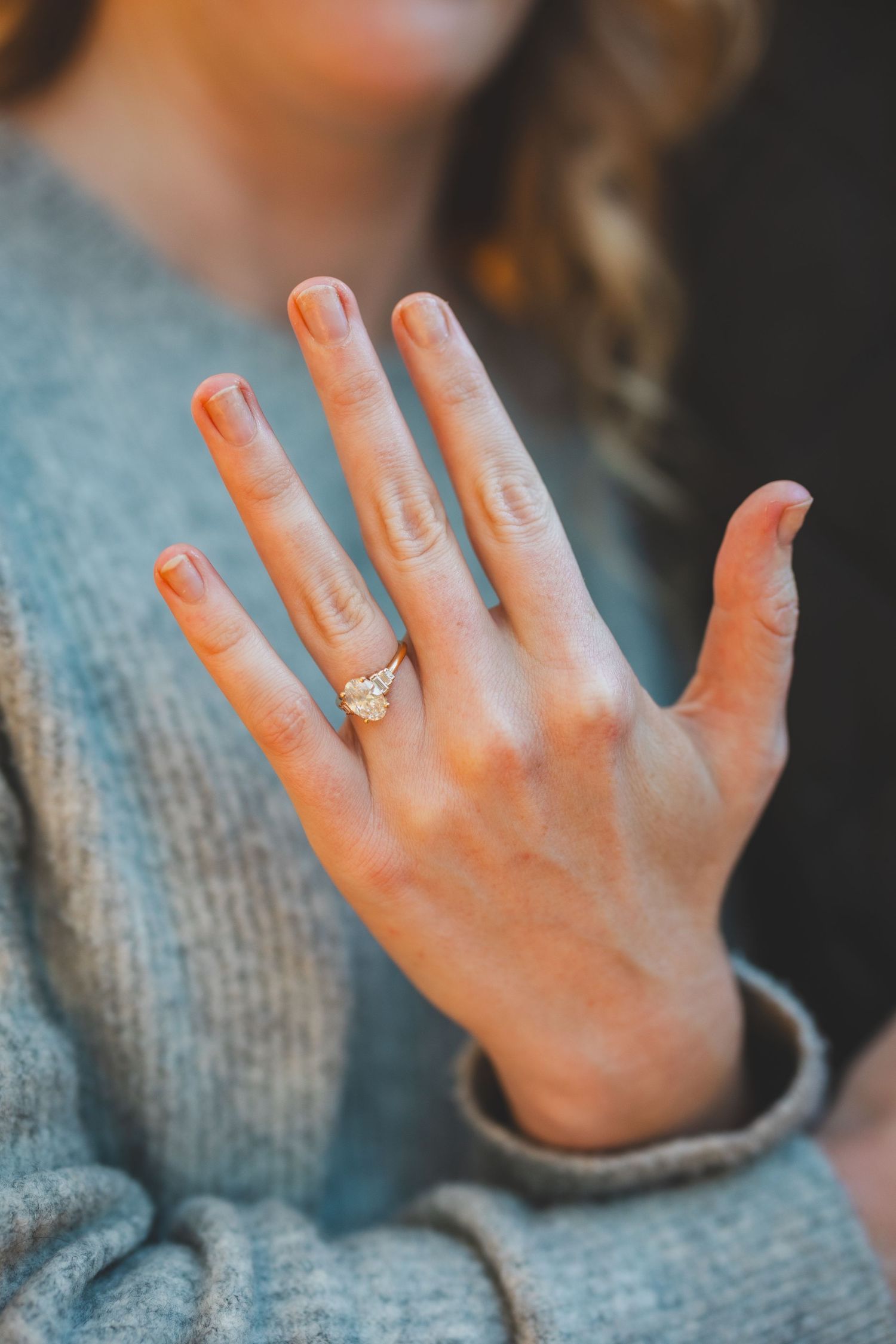 Close-up of a woman's hand displaying a gold diamond engagement ring while wearing a gray knit sweater.