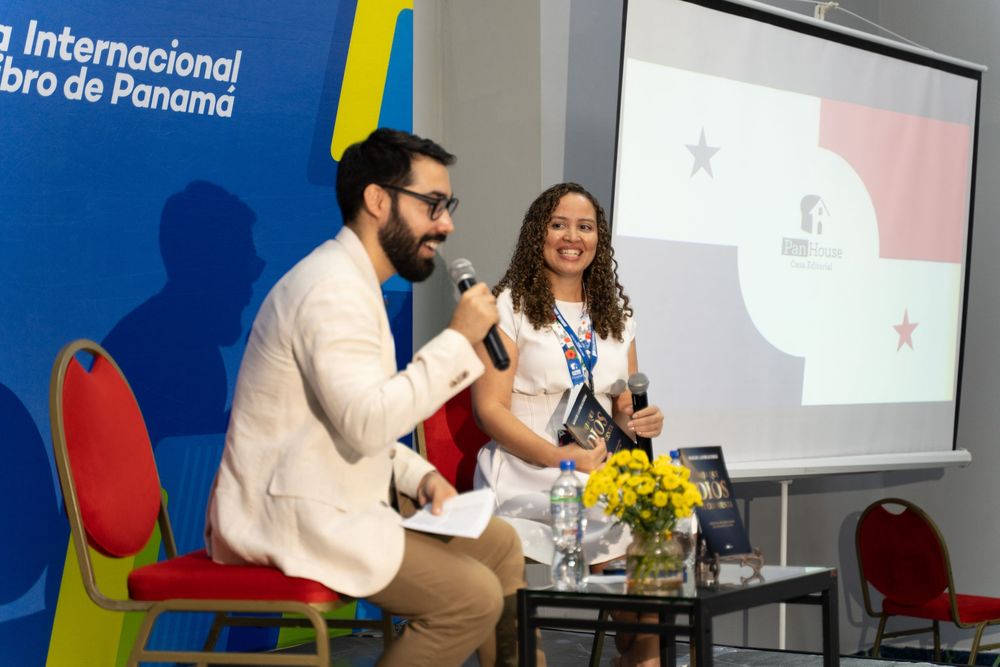 Two speakers at the Feria Internacional del Libro de Panama, seated on stage with a Panama flag displayed on screen.