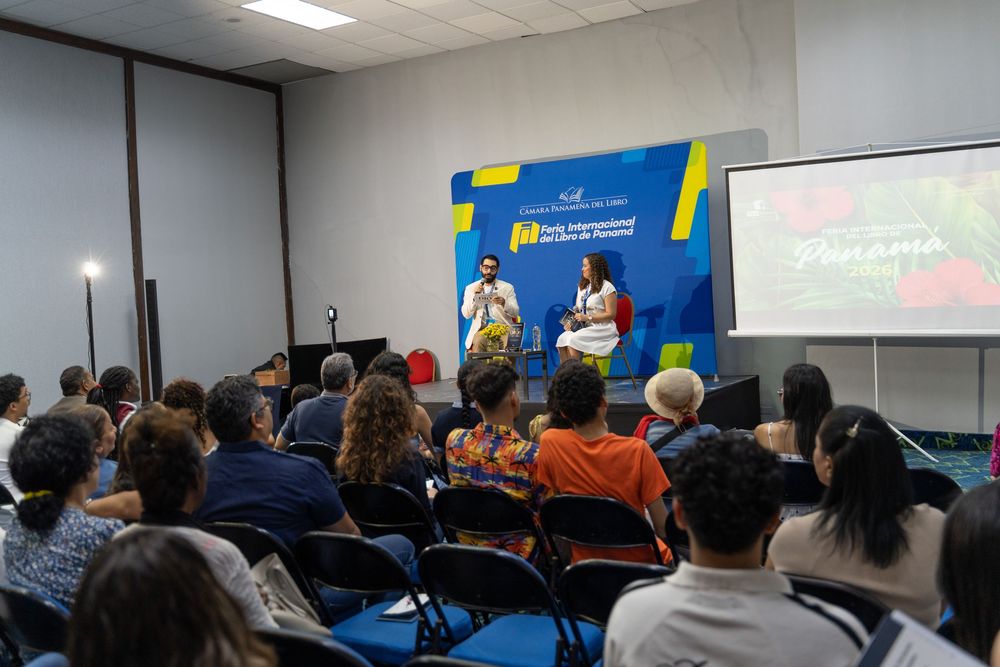 Two speakers present on stage at a Panama conference event with audience seated in blue chairs.