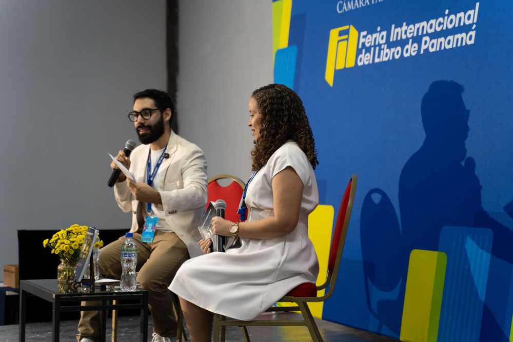 Two speakers at Feria Internacional del Libro de Panamá panel discussion, man in beige suit and woman in white dress.