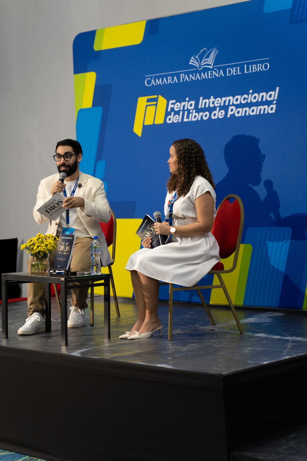 Two speakers on stage at Feria Internacional del Libro de Panamá, man with mic and woman in white dress.