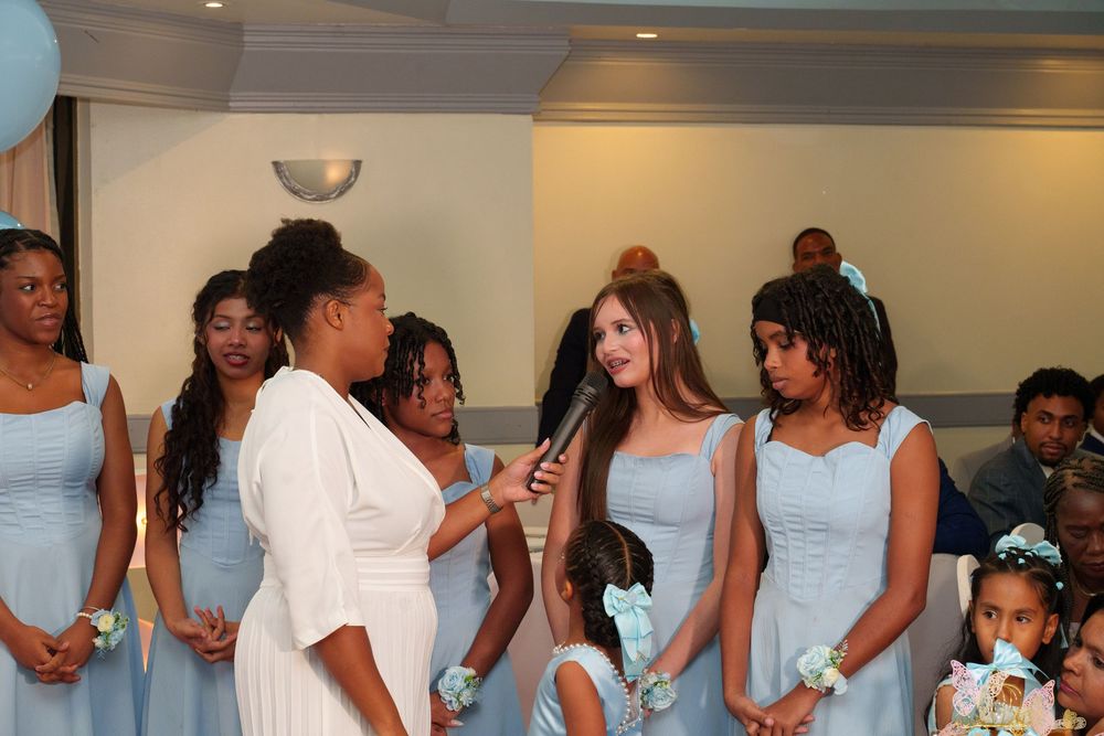 Bridesmaids in light blue dresses stand together during a wedding ceremony while a woman in white speaks.