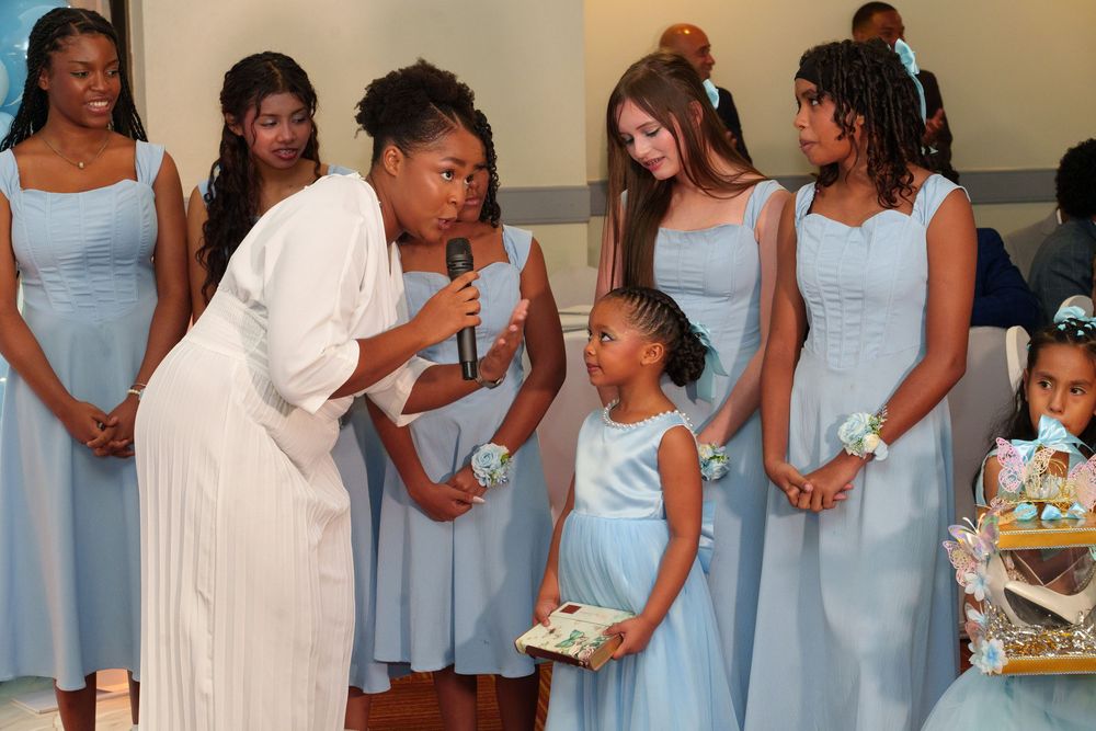 Woman in white dress speaks to bridesmaids in light blue gowns and flower girl at elegant wedding ceremony.