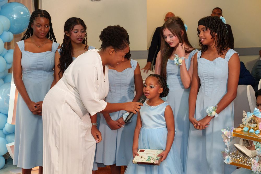 Women in light blue bridesmaid dresses gather around a young flower girl at an elegant wedding reception.