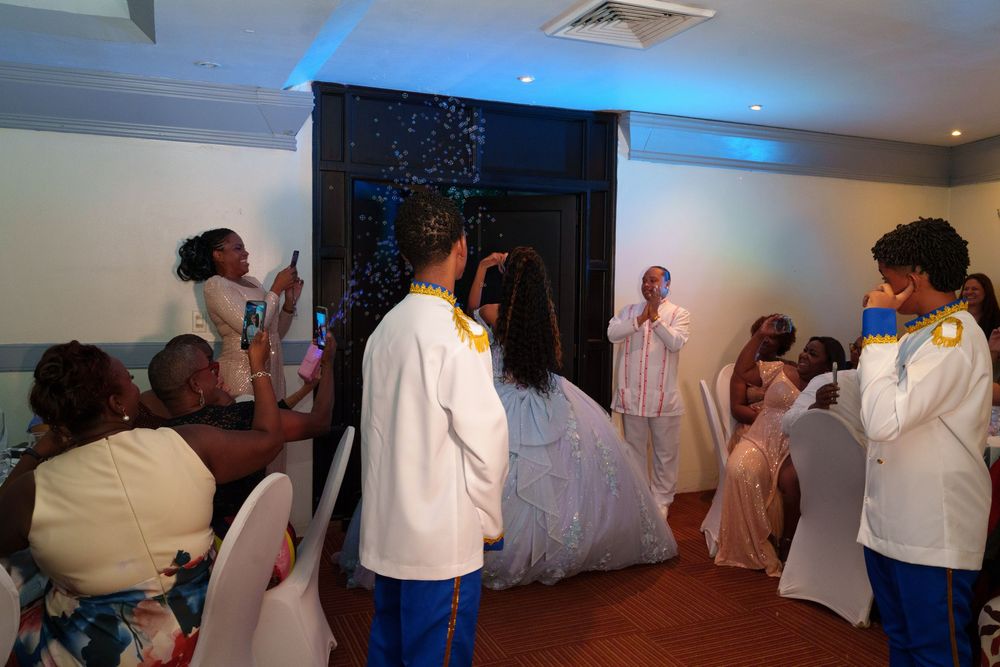 Guests photograph a bride in a white gown during an indoor wedding ceremony with blue ambient lighting.