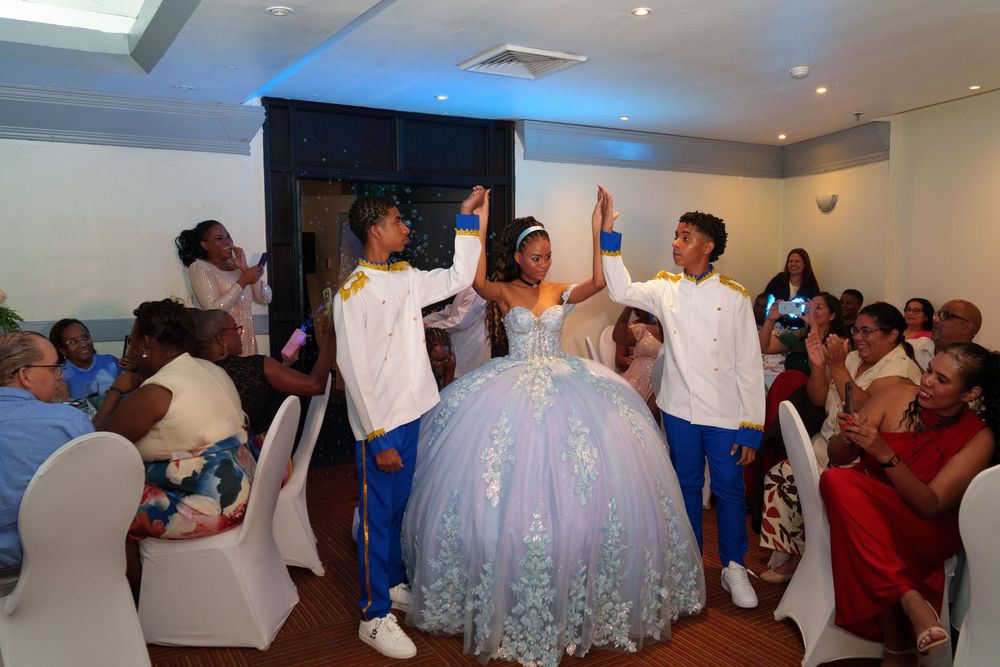 A young woman in a lavender quinceañera ball gown makes her grand entrance flanked by two escorts in white suits.